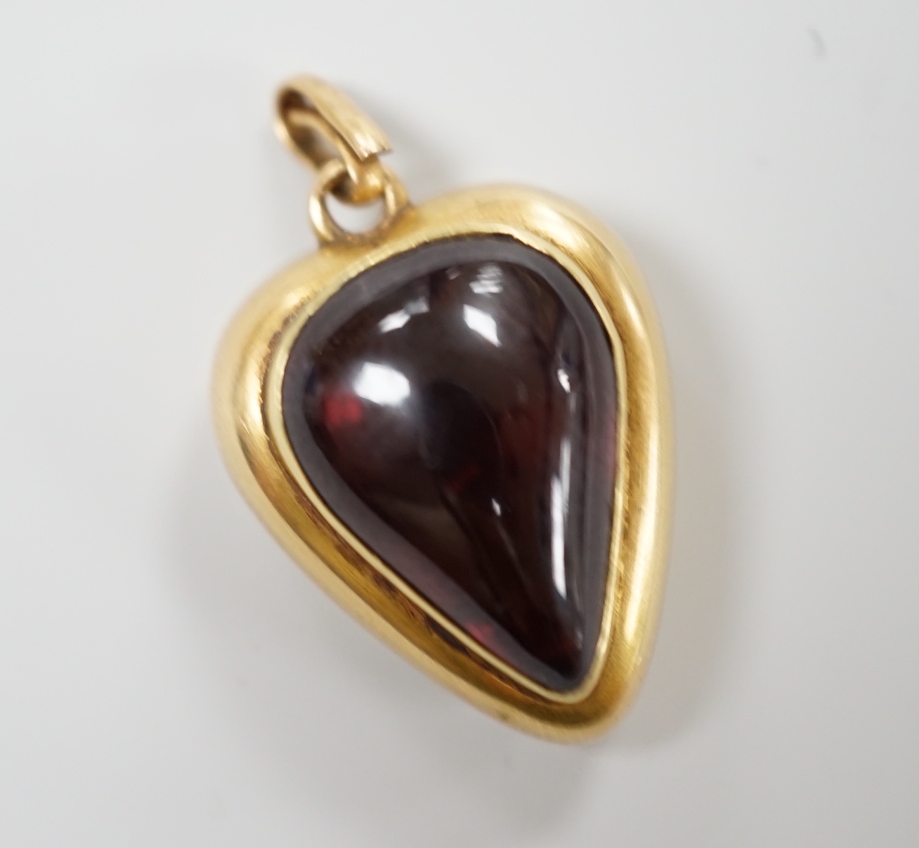 A late Victorian yellow metal (stamped 18) and cabochon garnet set heart shaped pendant, with glazed back, 22mm, gross weight 5.7 grams.
